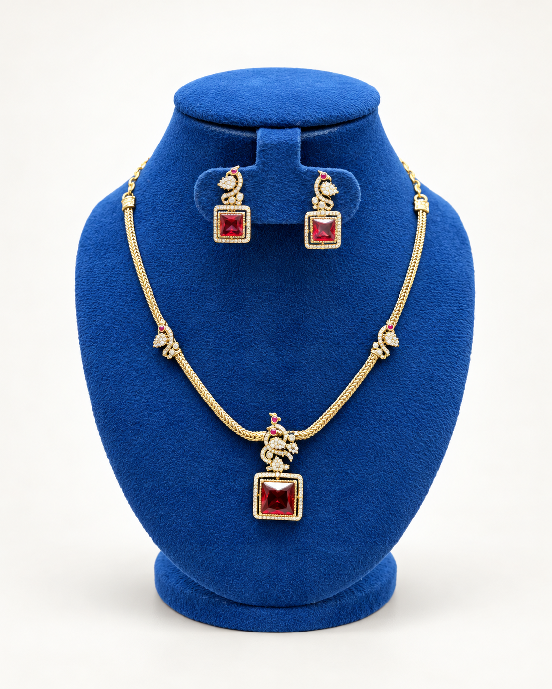 Kaveri peacock square stone necklace set with earrings in maroon on a blue velvet display stand