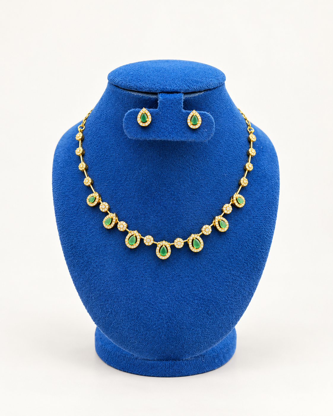 Kaveri teardrop station necklace set with stud earrings in green on a blue velvet display stand