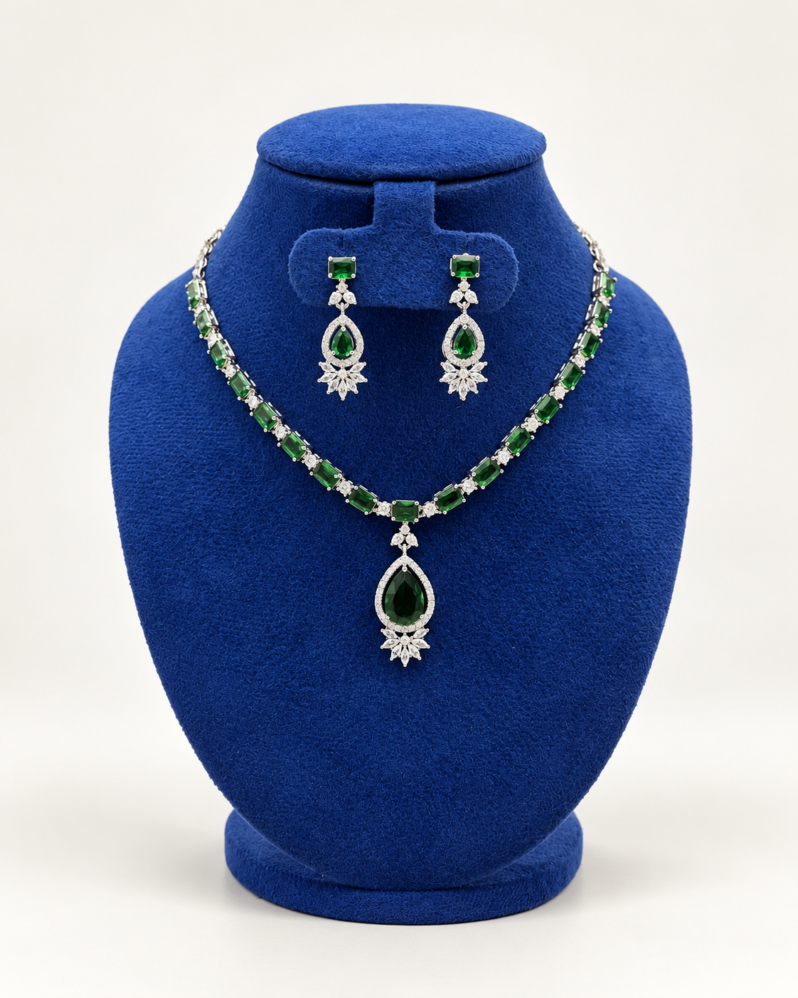Kaveri oval stone teardrop necklace set with earrings in green on a blue velvet display stand