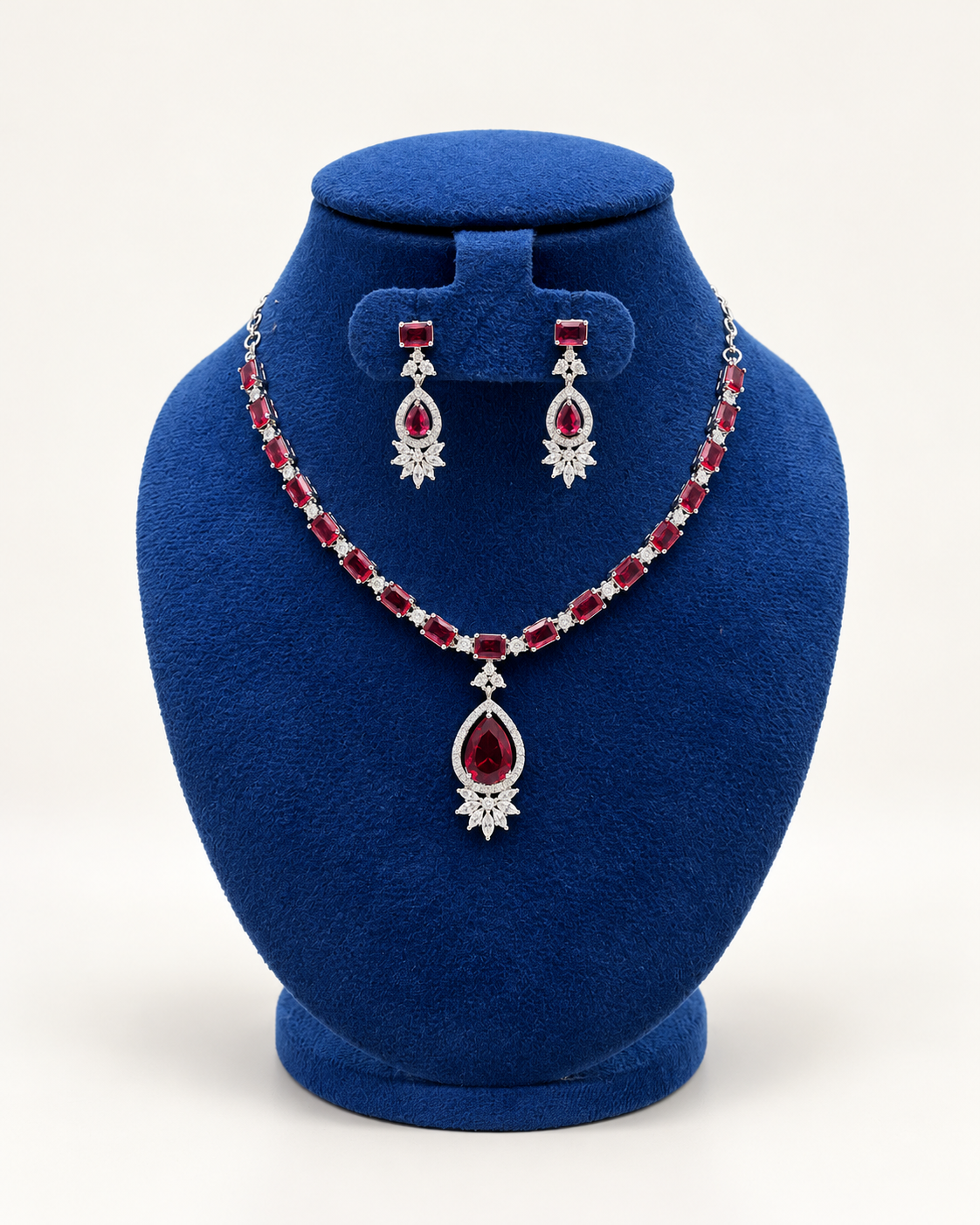 Kaveri oval stone teardrop necklace set with earrings in maroon on a blue velvet display stand